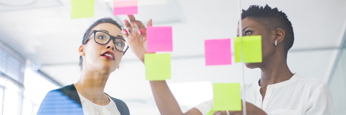Two Business Women in Training Discussing Data on Sticky Notes