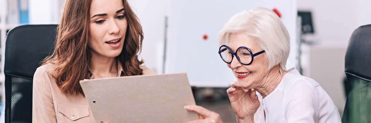 Woman Talking With Older Woman About Data on Clipboard