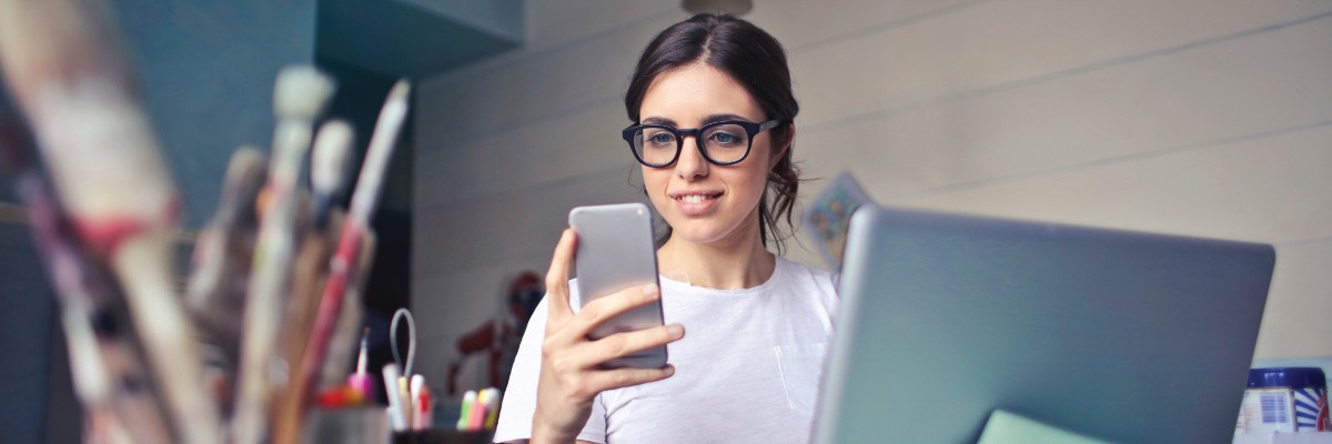 Woman At Computer Desk Looking At Phone Smiling